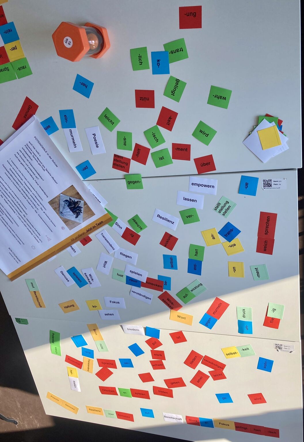 Tische voller bunter Wortkarten mit Silben, Vorsilben und Wörtern wie „Genuss", „Haltung", „Fokus", „Resilienz" – Material aus dem Sprachspiel
